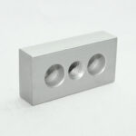 Silver metal block with three circular holes on one face, center hole threaded for fastener