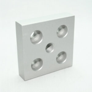 Square aluminum block with four circular holes and a central threaded hole, arranged in a 2x2 plus center pattern.