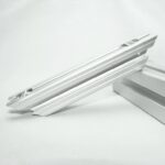 Close-up of a white aluminum extrusion rail with grooves, resting on a white surface on a neutral background.