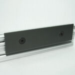 Close-up of a gray metal rail with a dark rectangular mounting plate secured by two screws along its length.