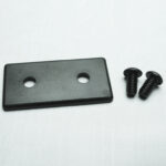 Rectangular black plastic plate with two holes beside two black screws on a white surface.