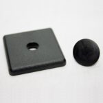 Close-up of a dark gray plastic block with a circular hole, resting on a white surface, with a black round knob nearby.