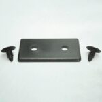Black rectangular metal plate with two circular holes, flanked by two black screws on a pale surface.