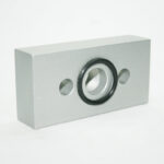 Silver rectangular metal block with a central threaded hole surrounded by a black ring and two small side holes.