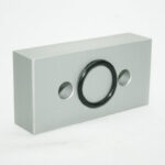 Rectangular metal mounting plate with a central circular rubber gasket and two side screw holes.