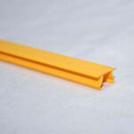 Close-up of a yellow plastic edging strip with a groove, resting on a pale surface.