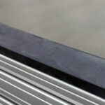 Close-up of a brushed metal surface with a dark seam and parallel horizontal grooves at the bottom.