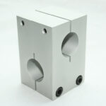 Gray plastic dual-terminal block with two round wire openings and screws on the front, used to secure two cables or conductors.