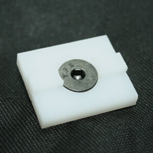White plastic clip with a circular metal washer/fastener centered on a dark fabric surface.