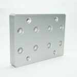 Rectangular aluminum mounting plate with a grid of round holes, some threaded for bolts.