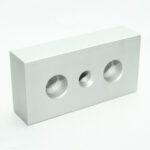 Silver rectangular metal block with three circular holes: two large, one threaded in the center on a white background.