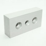 Metal rectangular block with three circular holes; the middle hole is threaded for a screw or bolt.