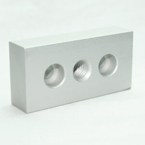 Rectangular gray metal block with three circular holes, the middle hole is threaded.