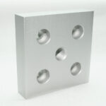 Silver metal block (machined aluminum) with five round holes: four empty and one central threaded bore, viewed at an angle against a white background.
