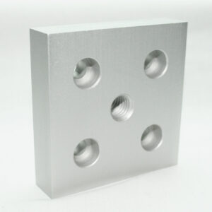 Silver metal block (machined aluminum) with five round holes: four empty and one central threaded bore, viewed at an angle against a white background.