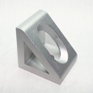 Silver metal triangular-prism block with a large circular hole through its top faces, resting on a light surface.