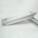 Set of silver aluminum profile rails with twin T-slot channels on each edge laid diagonally on a white background