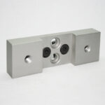 Metal modular block with two end caps and a central plate featuring threaded and non-threaded holes (industrial connector part).