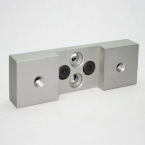 Metal modular block with two end caps and a central plate featuring threaded and non-threaded holes (industrial connector part).