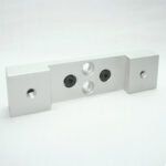 Silver aluminum mounting bracket with a central plate that has two recessed screws and two through-holes, flanked by square end blocks with through-holes each.
