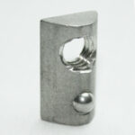 Small gray metal component with a circular through-hole and a silver ball detent on the side, photographed up close.