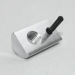 Metal block with a threaded hole and a black pin protruding from one end on a light surface.