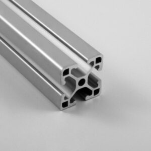 Close-up of a modular aluminum extrusion profile (T-slot framing) with hollow internal channels and rounded corners, shown at an angle for a structural framing context.