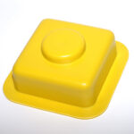 Close-up of a bright yellow plastic square tile with a central round boss/knob.