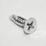 Close-up of a silver Phillips-head screw on a pale surface at an angle.