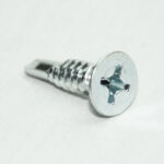 Close-up of a silver Phillips-head screw on a white background, showing the threaded shank and flat head.