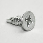 Close-up of a silver Phillips head screw lying on a light surface, showing threaded body and cross drive.