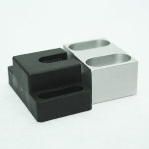 Close-up of a black plastic block and a silver metal block with two circular holes on a white background.