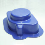 Blue plastic cap-like piece with a raised circular knob on top, photographed close-up.