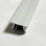 Close-up of a pale gray aluminum rail with a U-shaped channel at its end resting on a textured white surface